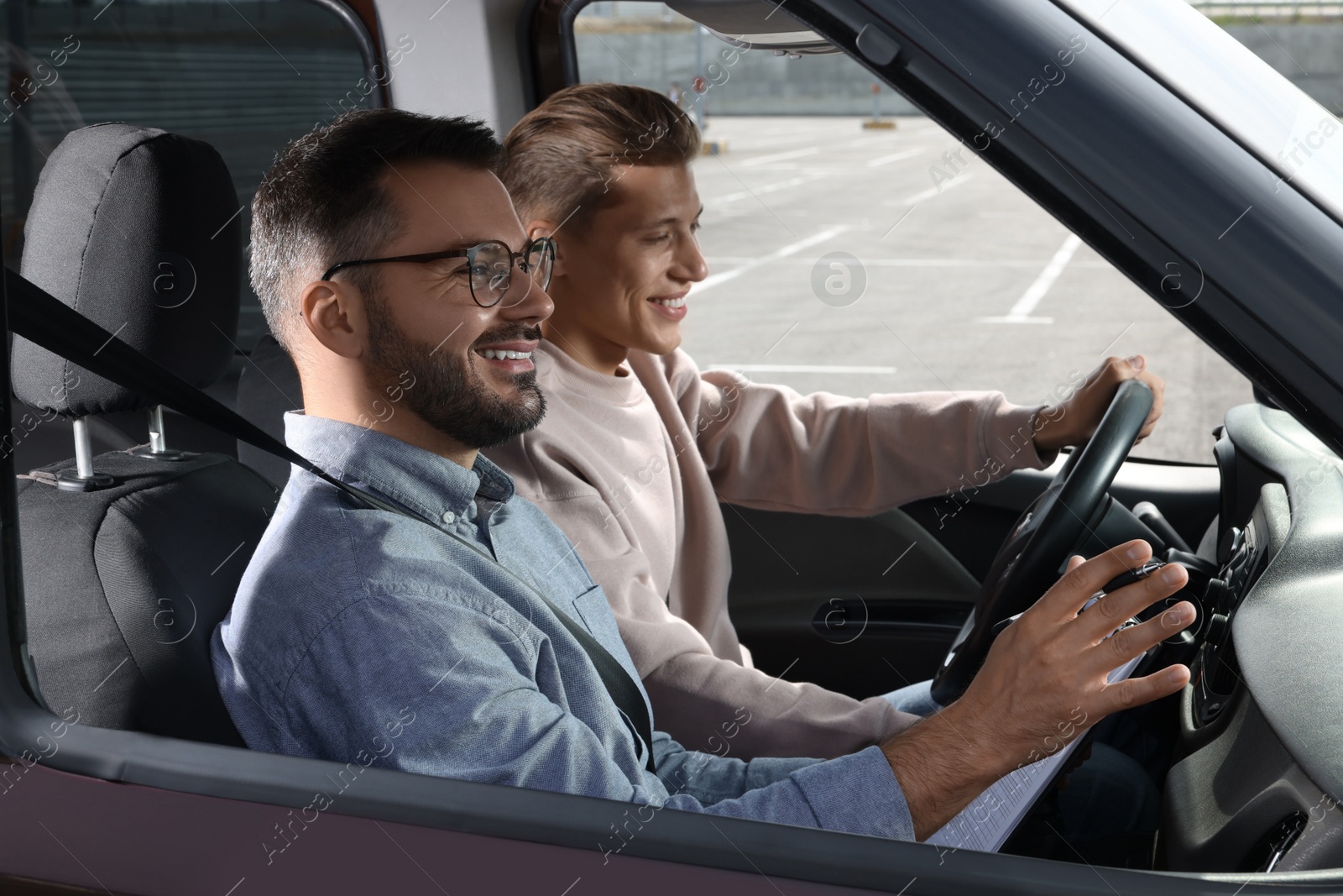 Photo of Driving school. Happy student passing driving test with examiner in car at parking lot