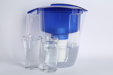 Filter jug and glasses with purified water on white background