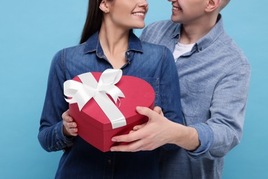 Photo of Boyfriend presenting gift to his girlfriend on light blue background, closeup