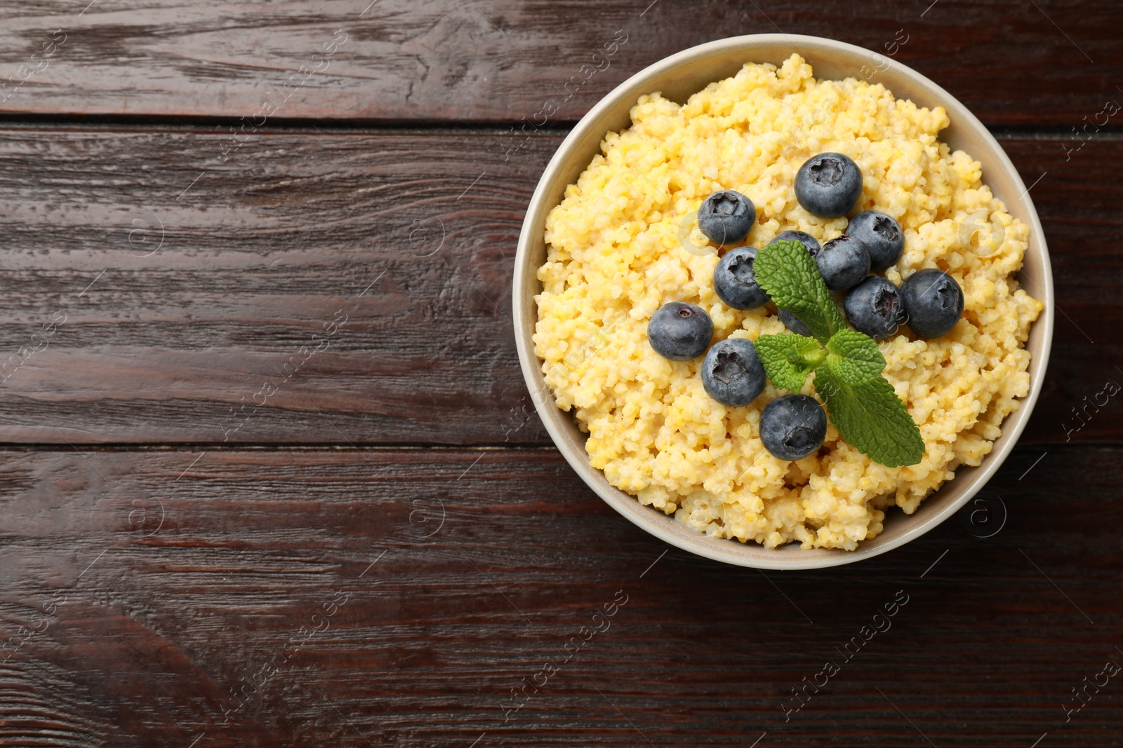 Photo of Tasty millet porridge with blueberries and mint in bowl on wooden table, top view. Space for text