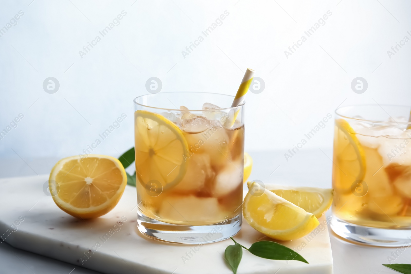 Photo of Glasses of lemonade with ice cubes and fruit on table against color background