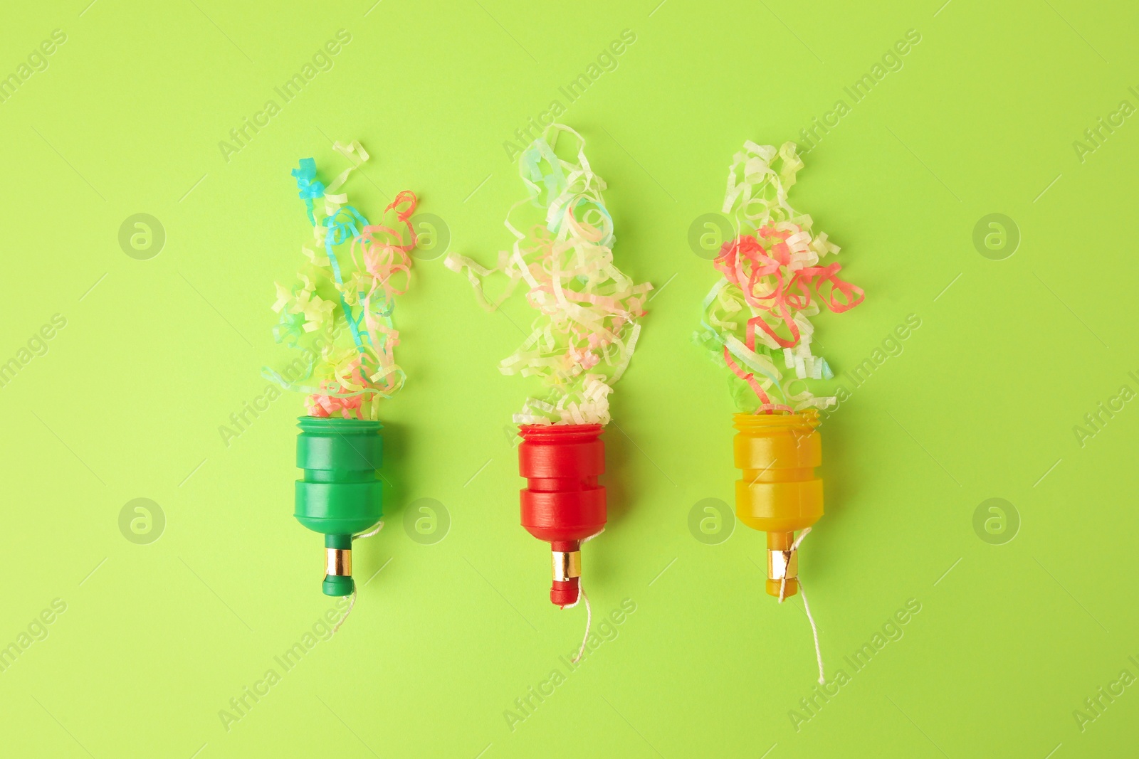 Photo of Beautiful serpentine bursting out of small party poppers on green background, flat lay