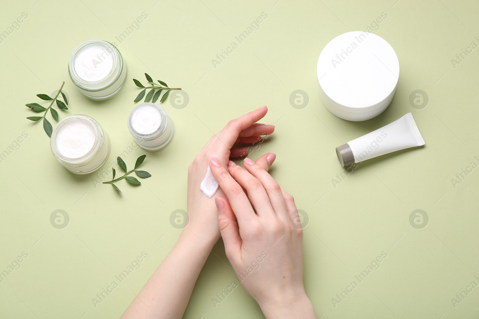 Photo of Woman applying hand cream on green background, top view