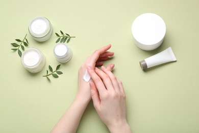 Woman applying hand cream on green background, top view