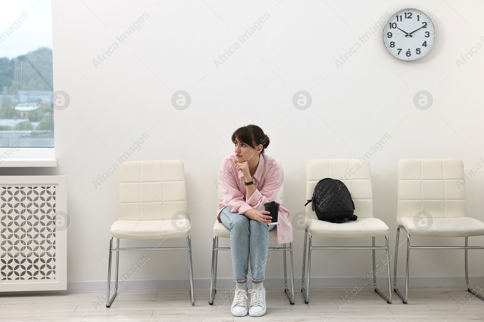 Photo of Woman with cup of drink waiting for appointment indoors