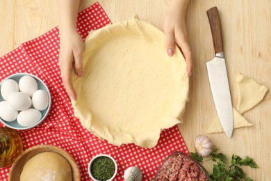 Woman making meat pie at wooden table, top view