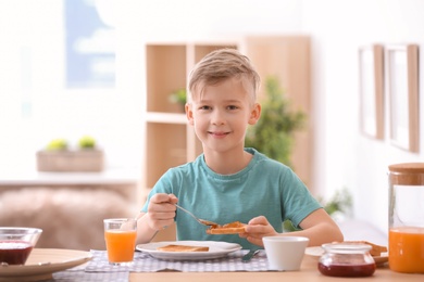 Photo of Cute little boy spreading jam onto tasty toasted bread at table