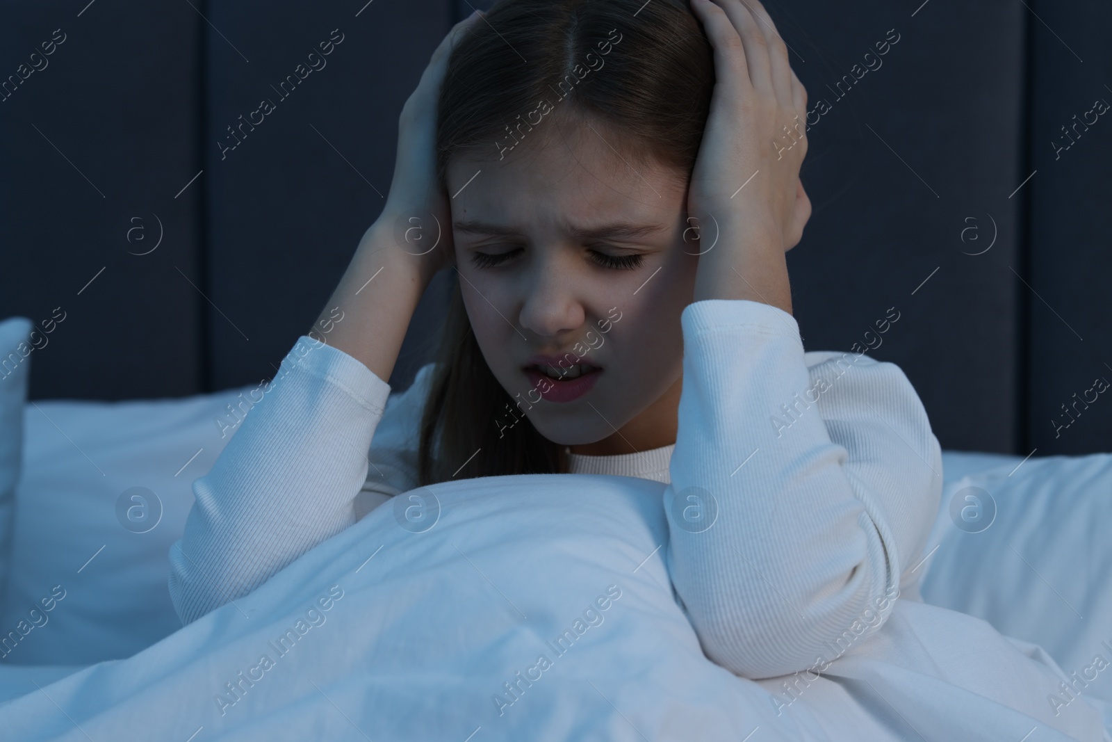 Photo of Little girl suffering from headache in bed at night