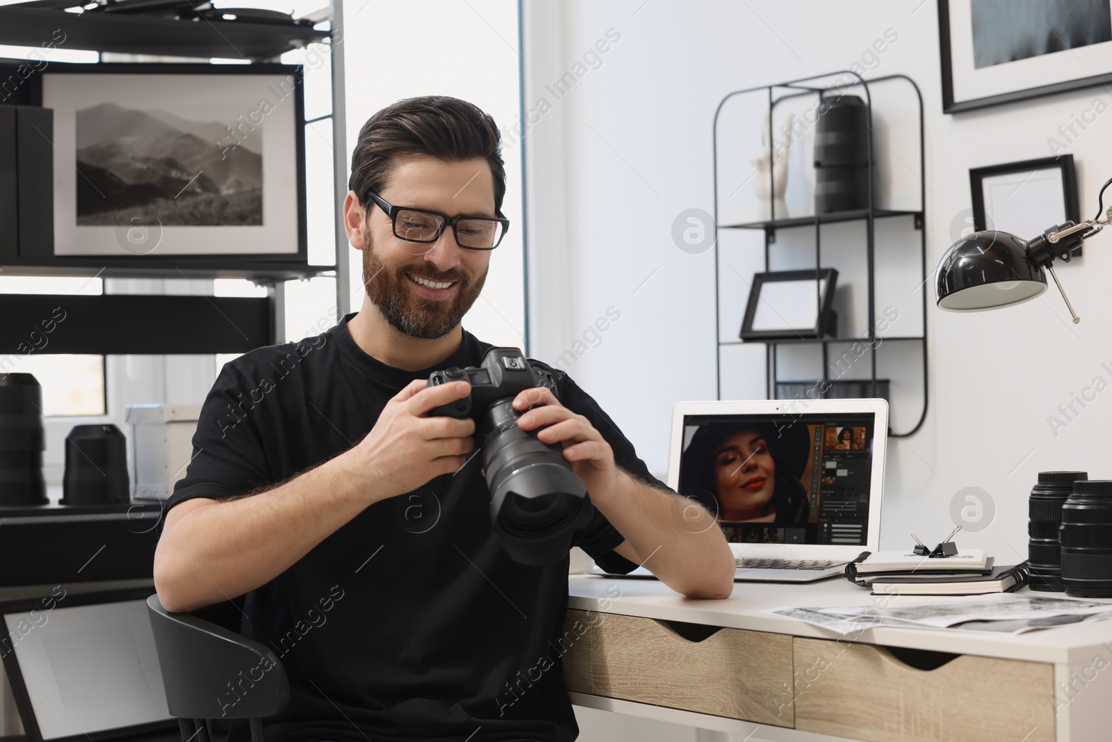 Photo of Professional photographer in glasses holding digital camera at table in office