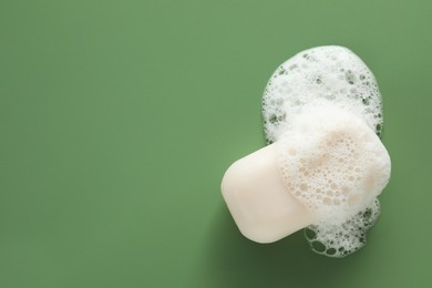 Soap bar with fluffy foam on green background, top view. Space for text