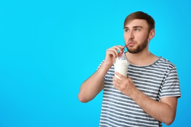 Photo of Young man with cup of delicious milk shake on color background