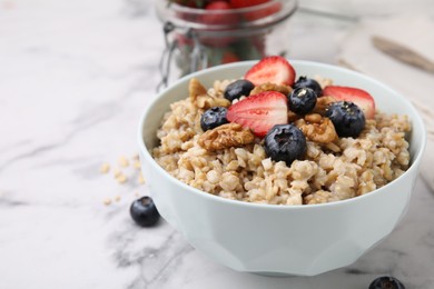 Photo of Tasty oatmeal with strawberries, blueberries and walnuts in bowl on white marble table, closeup. Space for text