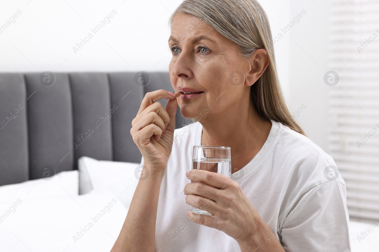 Photo of Beautiful woman taking vitamin pill in bedroom