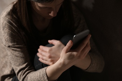 Photo of Sad woman using smartphone in dark room, closeup. Loneliness concept