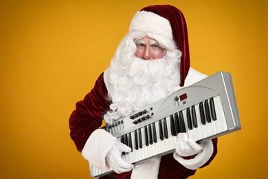 Photo of Santa Claus with synthesizer on yellow background. Christmas music