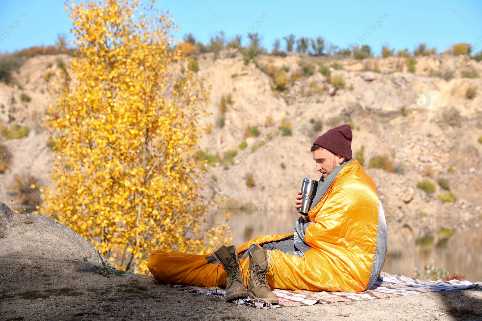 Photo of Male camper with thermos in sleeping bag outdoors. Space for text