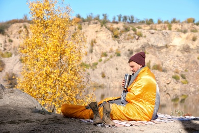 Male camper with thermos in sleeping bag outdoors. Space for text