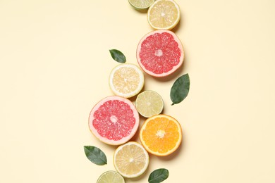 Different cut citrus fruits and leaves on beige table, flat lay