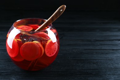 Photo of Glass bowl of delicious aromatic punch drink and ladle on black wooden table. Space for text