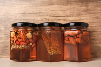 Photo of Jars with different nuts and honey on light table near wooden wall