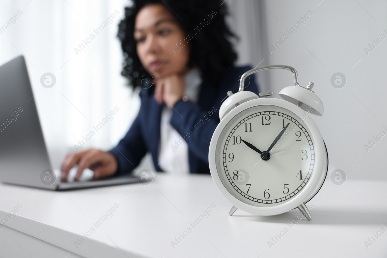 Photo of Stressful deadline. Alarm clock near woman working at white desk indoors, selective focus. Space for text