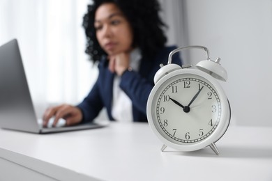 Photo of Stressful deadline. Alarm clock near woman working at white desk indoors, selective focus. Space for text