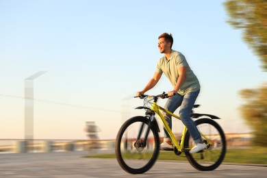 Image of Handsome young man riding bicycle on city waterfront, motion blur effect