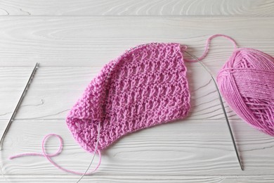 Soft pink yarn, knitting and metal needles on white wooden table, top view