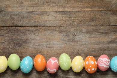 Photo of Flat lay composition of painted Easter eggs on wooden background, space for text