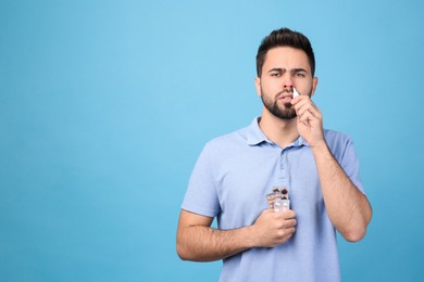 Photo of Man with pills using nasal spray on light blue background, space for text