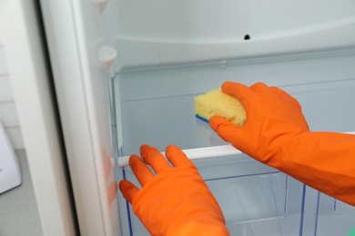 Photo of Worker in rubber gloves cleaning empty refrigerator, closeup