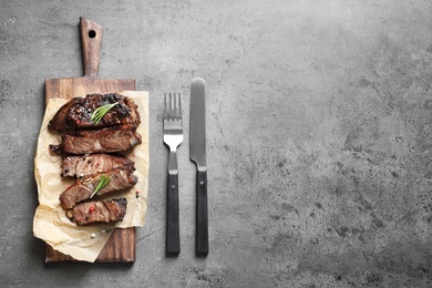 Photo of Flat lay composition with delicious barbecued meat served on gray table. Space for text