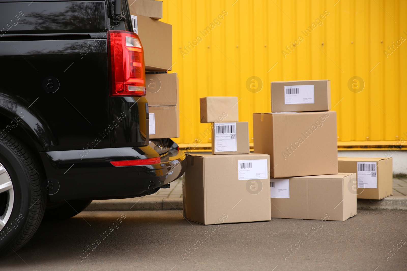 Photo of Black delivery van and many different parcels near yellow building outdoors. Courier service