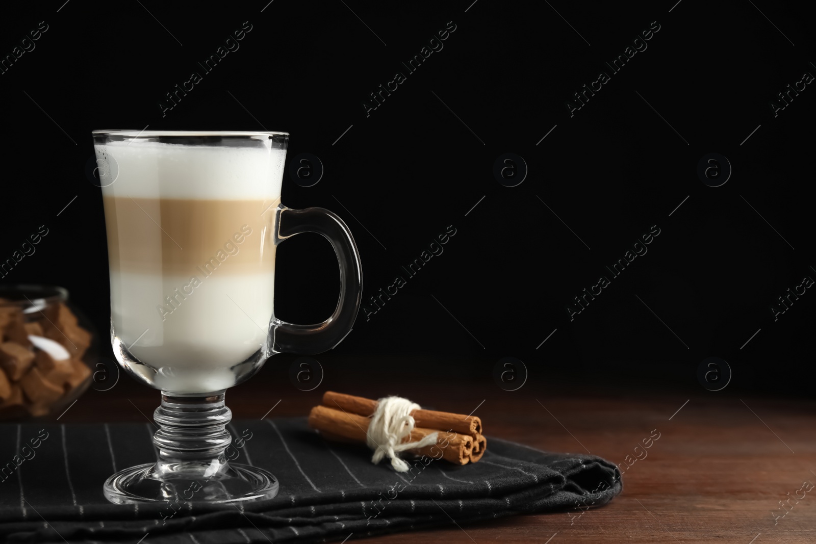 Photo of Delicious latte macchiato and cinnamon on wooden table against black background. Space for text