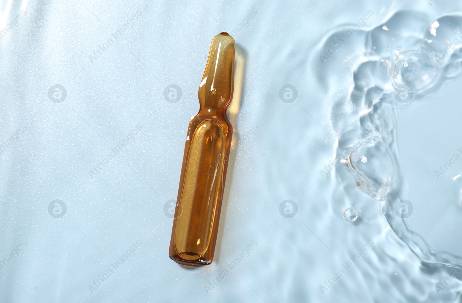 Photo of Skincare ampoule in water on light blue background, top view