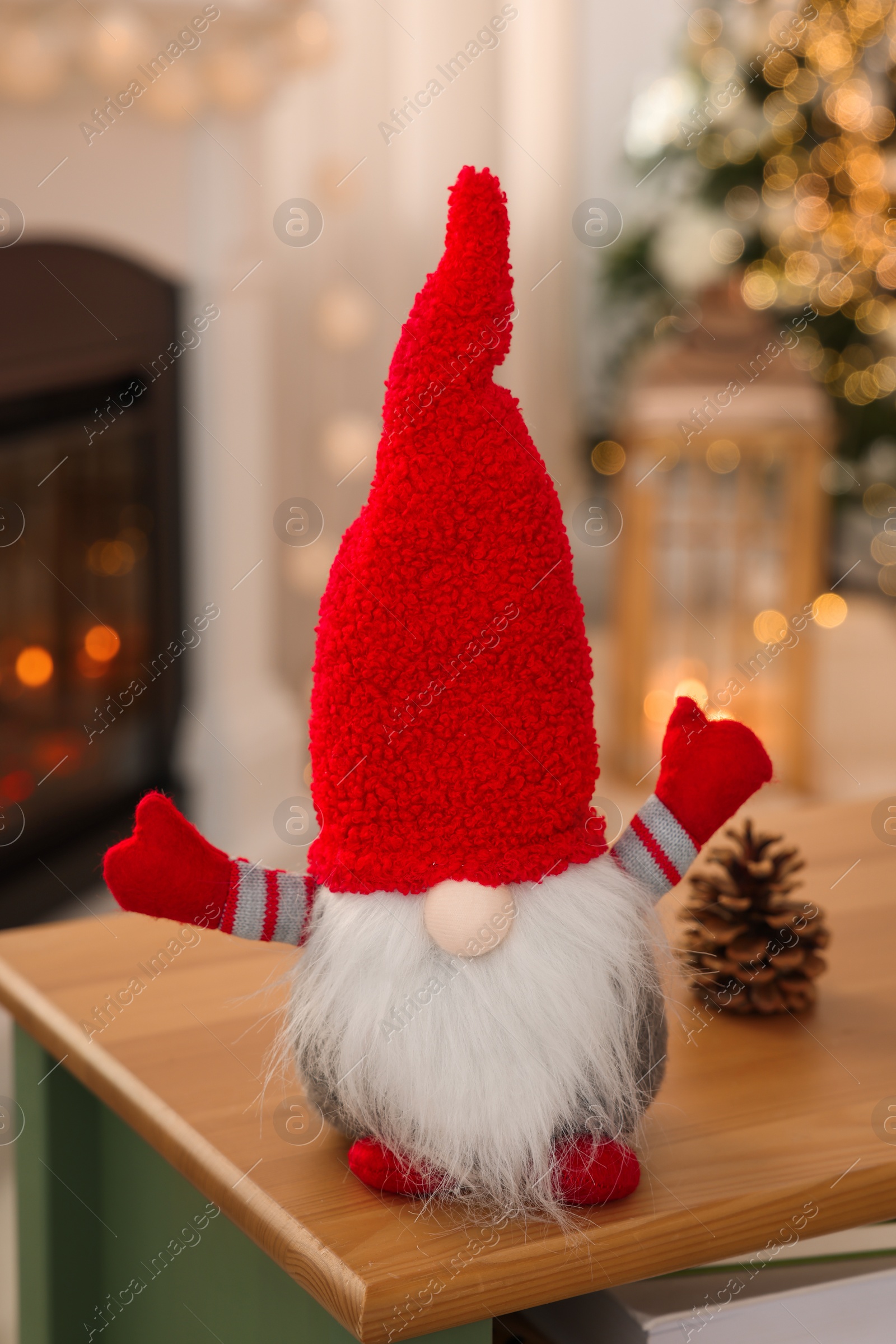 Photo of Cute Christmas gnome on wooden table in room with festive decorations