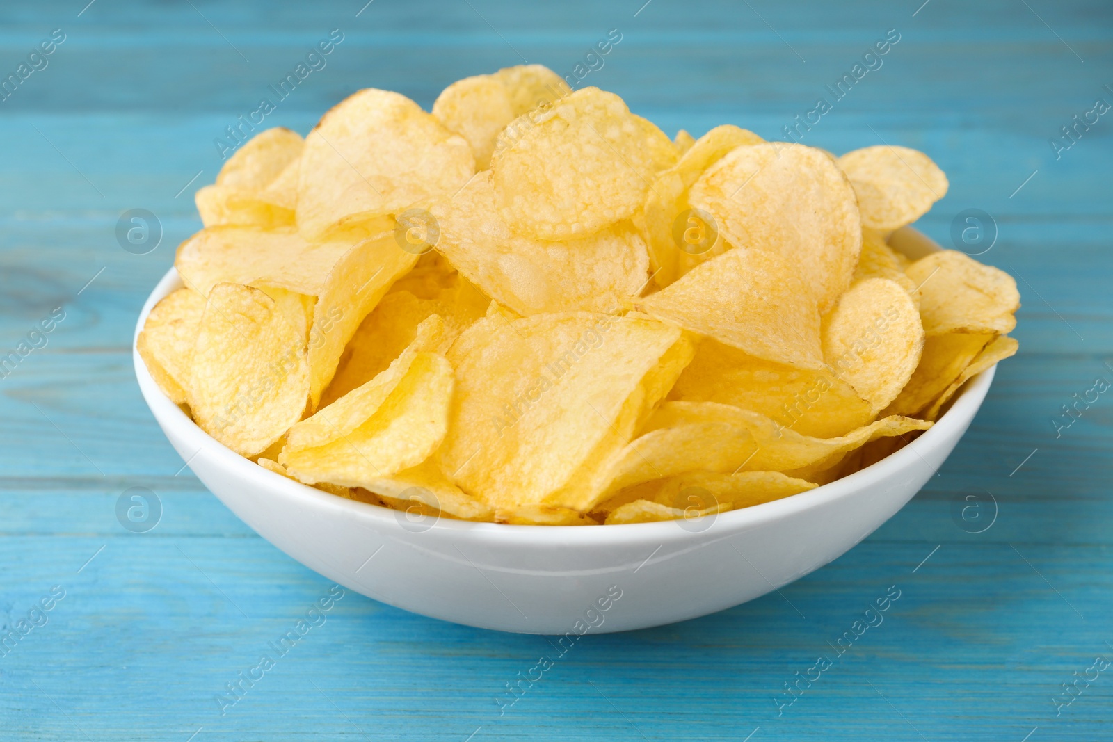 Photo of Bowl with delicious potato chips on light blue wooden table, closeup