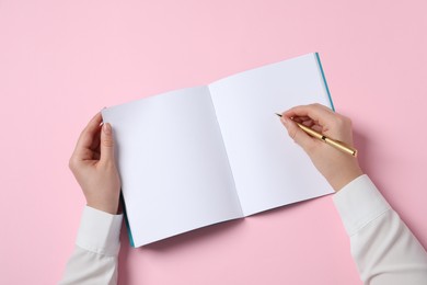 Woman with pen and notepad on pink background, top view