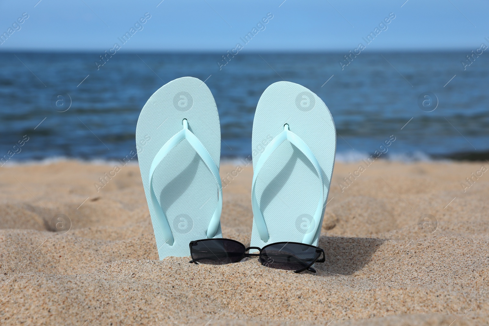 Photo of Stylish light blue flip flops and sunglasses on beach sand