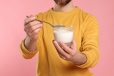Photo of Man with delicious yogurt and spoon on pink background, closeup