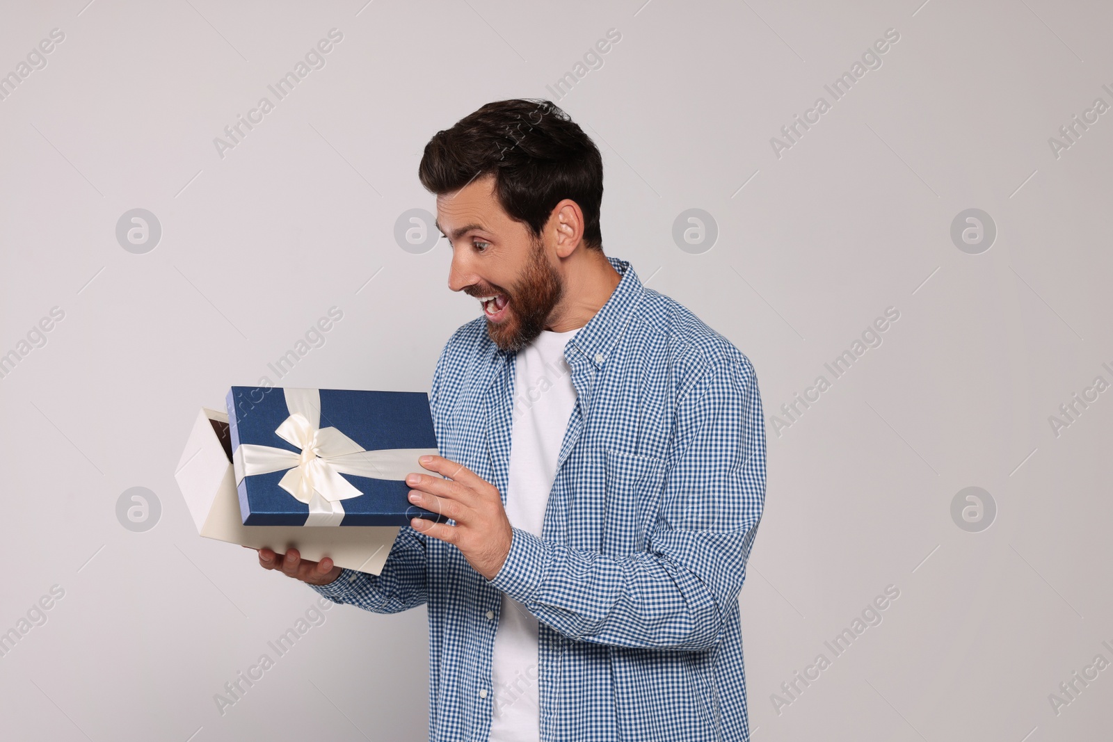 Photo of Emotional man opening gift box on light grey background