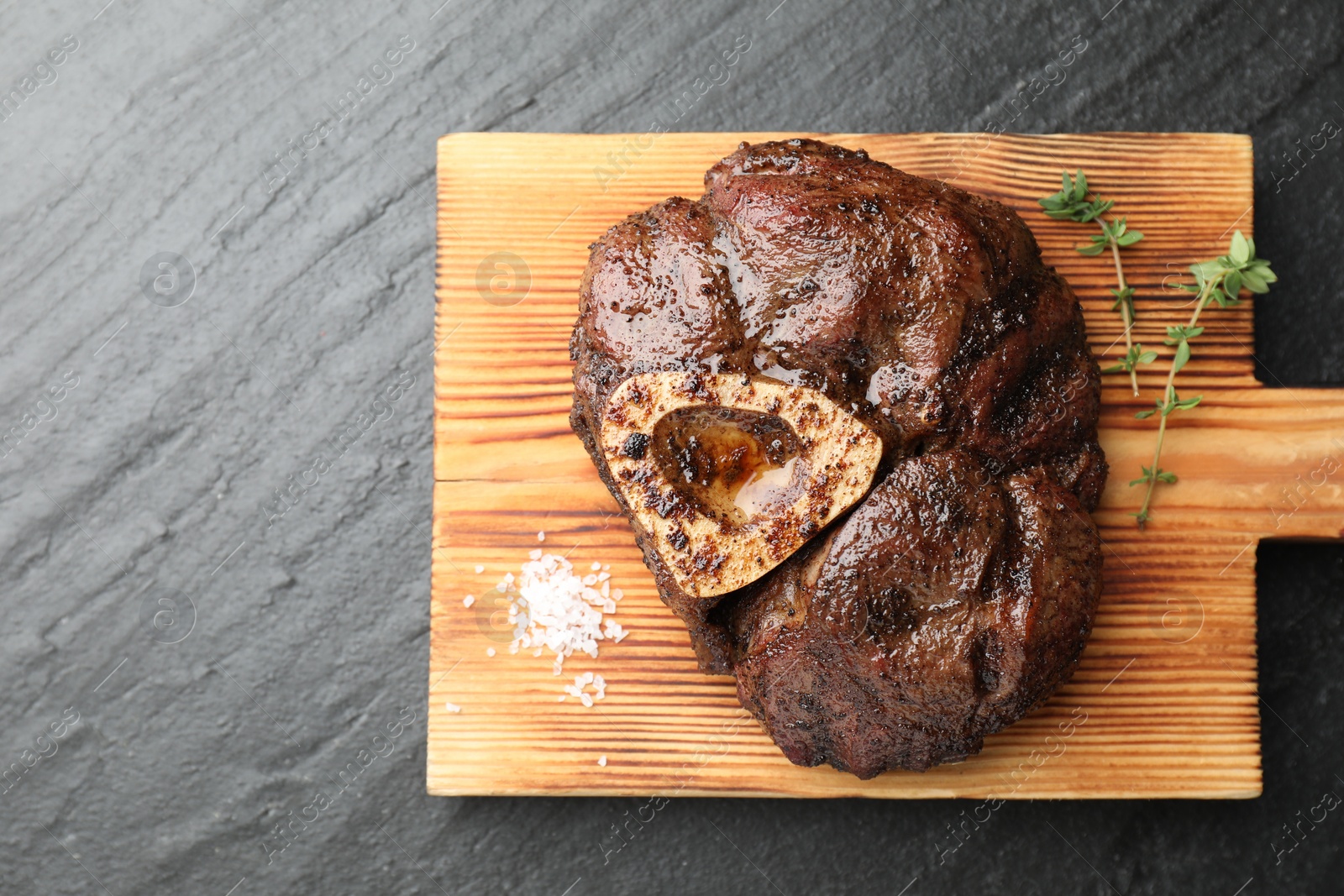 Photo of Piece of delicious grilled beef meat, thyme and salt on black table, top view. Space for text