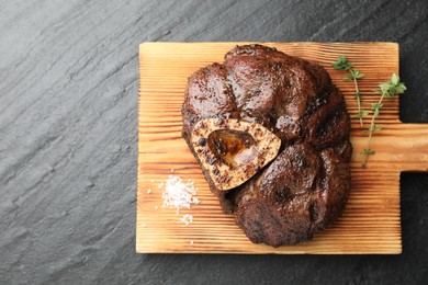 Piece of delicious grilled beef meat, thyme and salt on black table, top view. Space for text