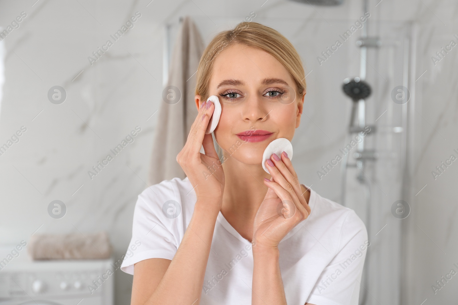 Photo of Happy young woman cleaning face with cotton pads in bathroom