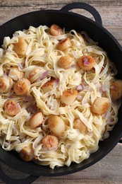 Delicious scallop pasta with onion in pan on wooden table, top view