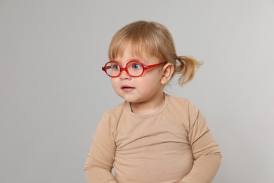 Cute little girl in glasses on light grey background. Space for text