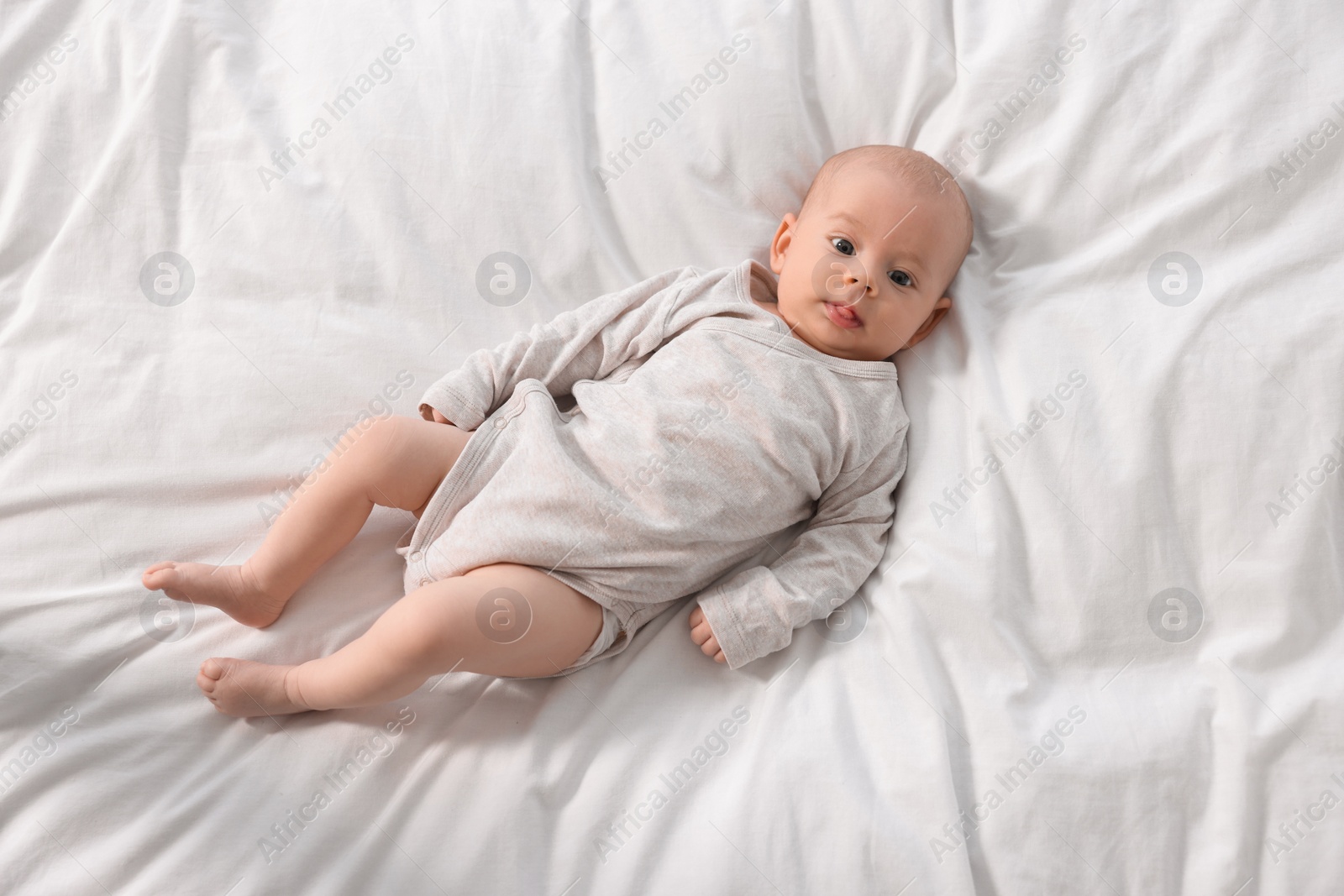 Photo of Cute little baby lying on white sheets, top view