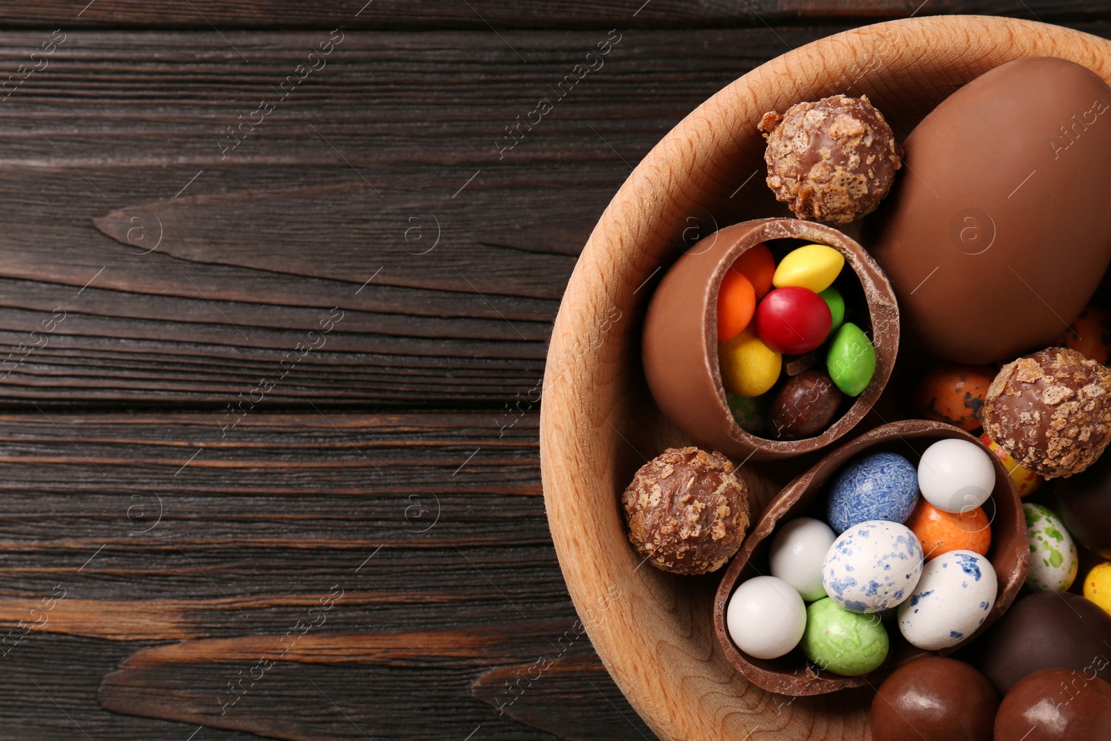 Photo of Tasty chocolate eggs and sweets in bowl on wooden table, top view. Space for text