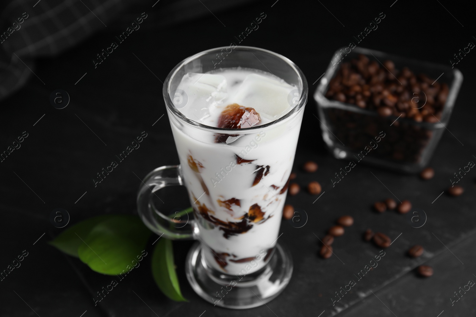 Photo of Glass cup of milk with delicious grass jelly and coffee beans on black table, closeup