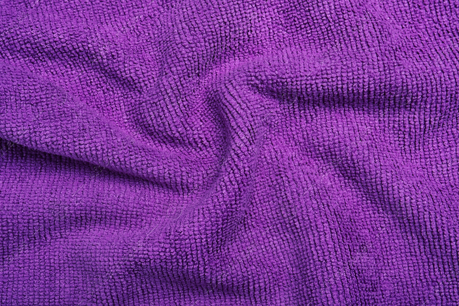 Photo of Crumpled purple microfiber cloth as background, closeup